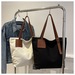 Detail of adjustable leather strap and logo patch on high-capacity canvas tote bag
