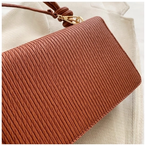 Detail of brown pleated handbag featuring vertical wave texture and gold metal buckle