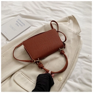 Close-up of brown pleated shoulder bag featuring knotted handle and gold metal hooks