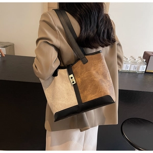 Detail view of a color-block tote bag with a gold metal buckle and leather shoulder strap
