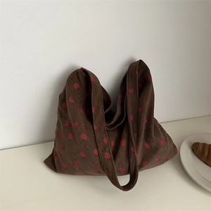 Brown corduroy shoulder bag with strawberry prints, shown on a table with a white plate