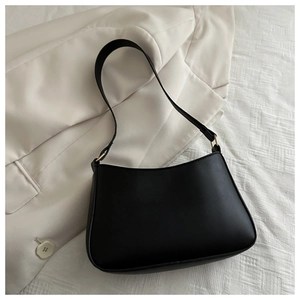 Gros plan du sac baguette en similicuir noir mat avec anneaux dorés sur fond de blazer blanc