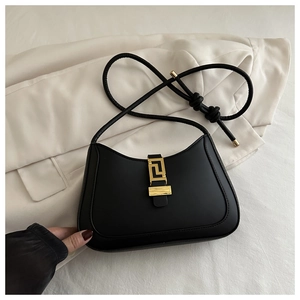 Detail of black leather hobo bag with a geometric gold metal buckle on a beige blazer