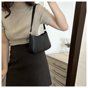Gros plan sur le sac à bandoulière en cuir noir mat avec boucle dorée porté par un mannequin