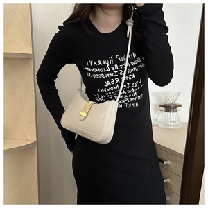 Detail view of cream shoulder bag featuring an ornate gold rectangular greca buckle