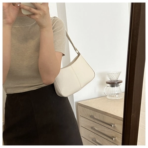Sac seau élégant en cuir blanc porté avec une tenue en maille beige minimaliste