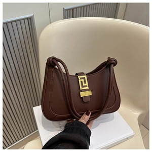 Detailed close-up of brown shoulder bag featuring Greek fret gold buckle and knotted straps