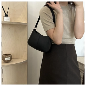 Gros plan sur un sac hobo minimaliste en cuir noir mat porté à l'épaule par un mannequin