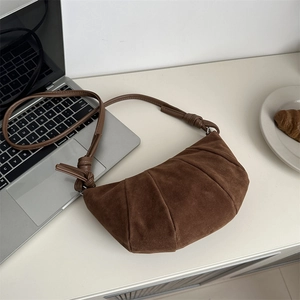 Vintage brown suede croissant shoulder bag with a knotted strap on a minimalist desk