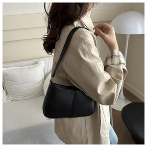 Détail d'un sac à bandoulière en cuir noir mat porté par un mannequin dans un salon épuré
