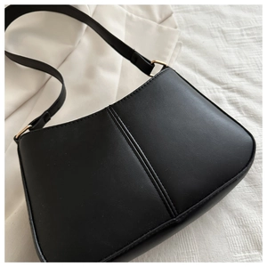Détail du sac bandoulière noir en cuir PU avec couture verticale et boucle dorée