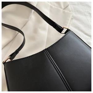 Détail d'un sac en cuir noir mat avec boucle dorée et couture verticale décorative