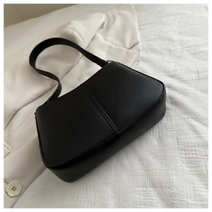 Détail du sac sous l'aisselle en similicuir noir avec couture verticale sur costume blanc