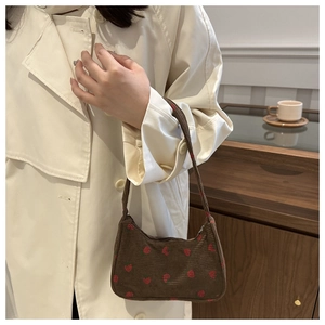 Détail d'un sac sous le bras en velours côtelé à fraises avec un trench-coat blanc