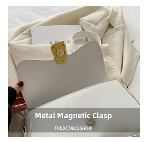 Detail view of the secure gold hardware magnetic buckle on a white leather baguette bag