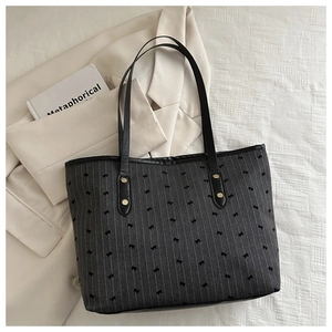 Detail of a black striped tote bag with bows, styled with a blazer and book
