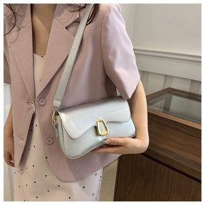 Detail of silver metallic shoulder bag featuring a gold horseshoe buckle on light suit