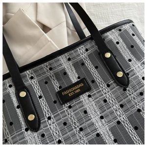 Macro detail of black polka dot mesh, lace stripes, and leather logo plate on tote bag