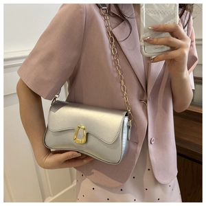 Detail of silver flap crossbody bag with gold trapezoidal clasp and fine chain strap