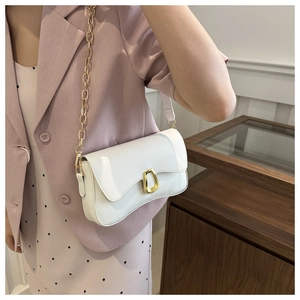 Close-up of white leather crossbody bag featuring gold buckle and chain strap on a model