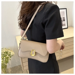 Detail of beige leather shoulder bag featuring a prominent gold horseshoe buckle decoration
