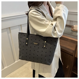 Detail of dark grey canvas tote with bow patterns, leather straps and gold metal plaque