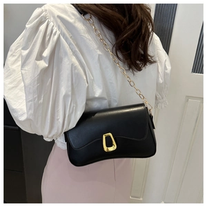 Detail of a black synthetic leather crossbody bag with a gold chain and geometric clasp
