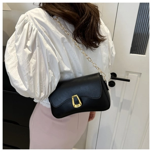 Detail of black leather crossbody bag featuring gold chain strap and geometric buckle