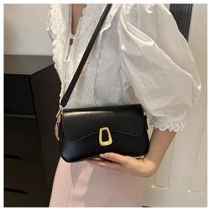 Close-up of black leather crossbody bag with a gold geometric clasp on a female model