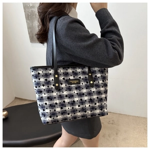 Close-up of heart patterned plaid tote bag with black leather straps and brand label