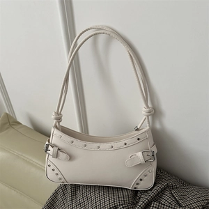 Cream vintage underarm bag with silver rivets and double buckle straps in a minimalist room