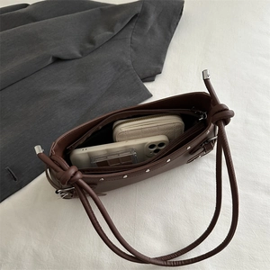Brown leather underarm bag with silver rivets and knot strap showing internal capacity