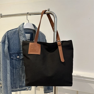 Minimalist black canvas tote bag with brown leather handles and adjustable metal buckle
