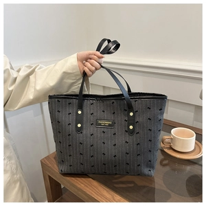 Detail of grey canvas tote bag featuring small black bow embroidery and brand leather patch