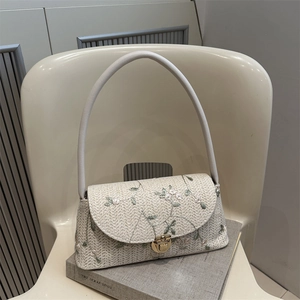 Straw woven shoulder bag with floral embroidery and gold metal lock on white chair