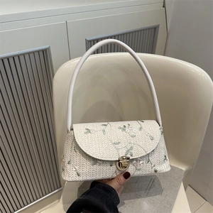 Straw shoulder bag with floral lace embroidery and golden clasp on beige woven texture