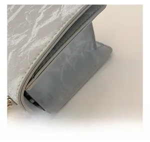 Detail shot of grey textured small square bag showing fine side stitching and chain strap