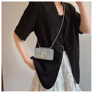 Detail of grey mini crossbody bag with gold keyhole clasp and thin metal chain strap