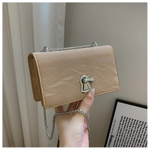 Close-up of beige wrinkled leather crossbody bag with silver lock and chain strap