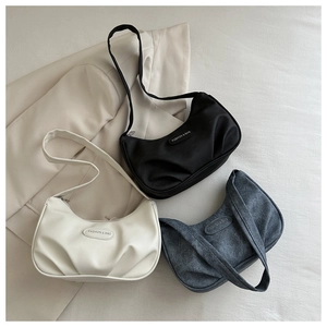 Minimalist pleated crescent bags in black, beige, and blue shown on a beige blazer