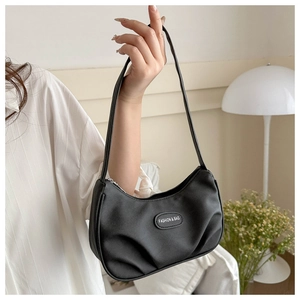 Close-up of black ruched crescent underarm bag with metal logo detail held by model