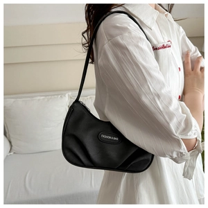 Detail shot of black pleated crescent bag featuring an oval fashion logo nameplate