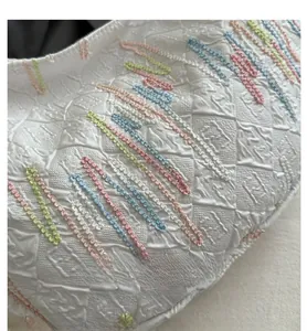 Detail of white quilted handbag featuring colorful wave embroidery and textured fabric