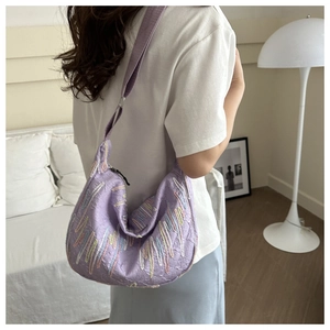 Close-up of purple crescent shoulder bag featuring colorful wavy embroidery and wide fabric strap