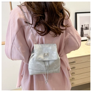 Detalle de una mochila plateada con hebilla de mariposa y correas de cadena en un modelo