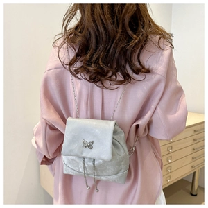 Detalle de mini mochila de terciopelo plateado con correas de cadena y mariposa