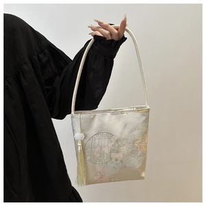 Detailansicht der beigefarbenen Brokat-Beuteltasche mit Blumenmustern und Quastenanhänger