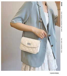 Close-up of quilted cream crossbody bag with metal chain strap and decorative sphere charm
