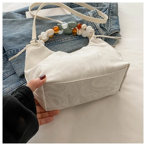Detail of white marble textured half-moon bag with colorful beaded handle on denim