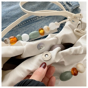 Detail of white pleated bucket bag featuring colorful beaded handle and magnetic closure